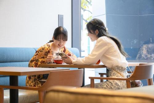 two women sitting at tables looking at a cell phone at The Royal Park Canvas - Kobe Sannomiya in Kobe