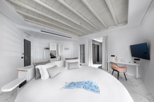 a white bedroom with a large white bed and a desk at Deliades Hotel in Ornos