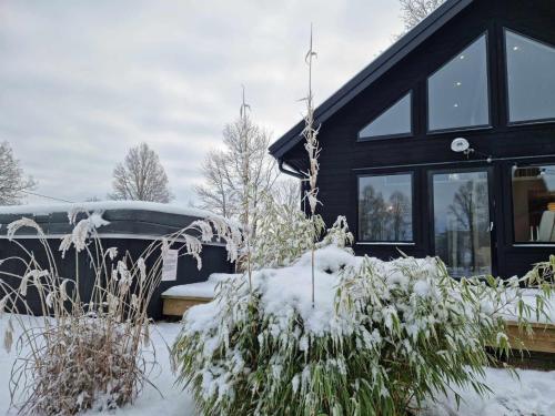 a black house with snow on the front of it at Newly built cottages with jacuzzy and sauna in Älmhult