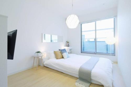 a white bedroom with a large bed and a window at b hotel Ball Park - Apt 2mins to Baseball 5mins to Hiroshima Sta in Hiroshima