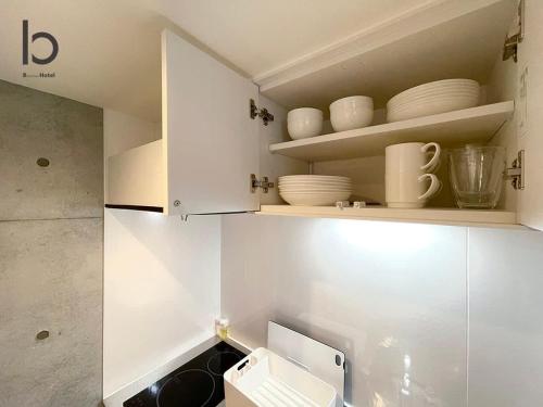 a kitchen with white cabinets and a sink and dishes at bHOTEL Nekoyard - Modern Loft Studio Near Peace Park & City Center in Hiroshima
