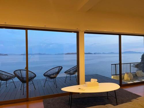 a room with chairs and a table and a view of the water at bLOCAL Sugawa House - Exclusive Seaside Escape in Ocean House in Kure
