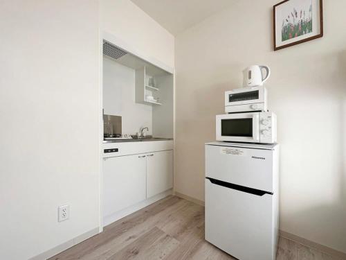 尾道的住宿－bHOTEL Yutori - Attractive 1Br Apt for 4 people in Onomichi，白色的厨房配备了微波炉和冰箱。