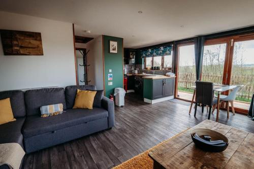 a living room with a blue couch and a kitchen at Woodpecker Lodge- A Pet Friendly Rural Retreat in Callington