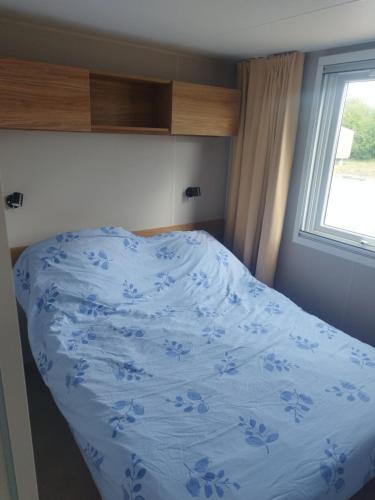 un lit dans une chambre avec un couvre-lit bleu avec une fenêtre dans l'établissement Mobil-home bord de mer, à Colleville-sur-Mer