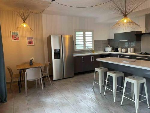 a kitchen with a refrigerator and a table and chairs at Ocean-Villa 12 personnes avec piscine à 50m de la plage de l'Etang Salé Les Bains in Étang-Salé les Bains