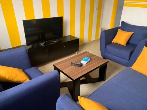 un salon avec des chaises bleues, une table et une télévision dans l'établissement Résidence l'endroit, à Abidjan