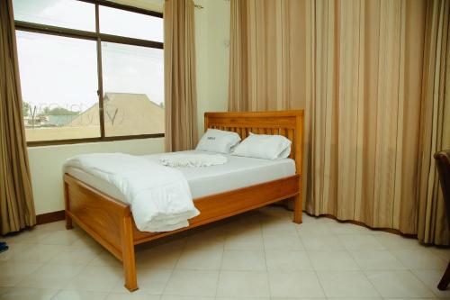 a bedroom with a bed with white sheets and a window at FQ Hotel Limited in Dar es Salaam