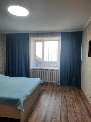 1 dormitorio con 1 cama con cortinas azules y ventana en Сдам 1-комн квартиру в Центре, en Semey