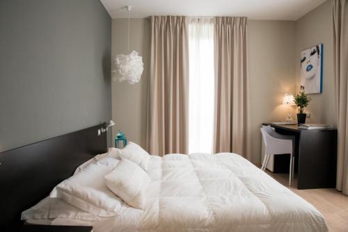 a bedroom with a white bed with a desk and a window at Berghotel in Bergamo