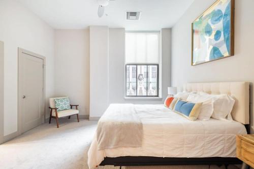 a white bedroom with a large bed and a chair at 2BR Distinguished Apartment Rooftop Deck & Gym in Baltimore