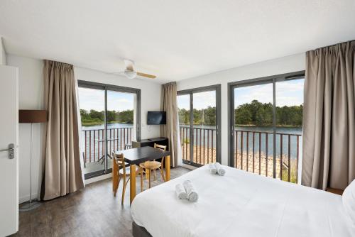 um quarto de hotel com uma cama, uma secretária e janelas em All Suites La Teste – Bassin d’Arcachon em La Teste-de-Buch