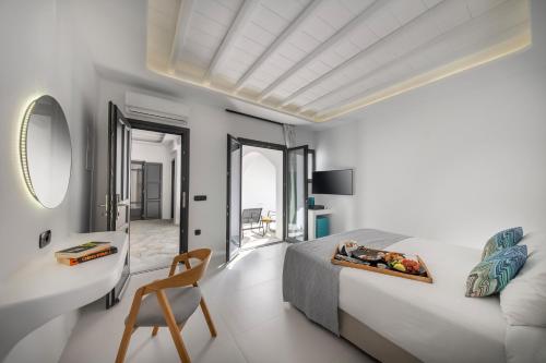 a white bedroom with a bed and a chair at Deliades Hotel in Ornos