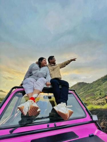 a man and woman sitting on the back of a pink truck at jeep tour sunrise batur in Kintamani