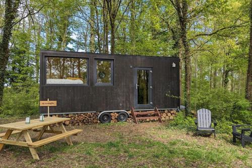 ein schwarzes winziges Haus im Wald mit einem Picknicktisch in der Unterkunft Tiny House La Clairière au milieu des bois ! in Sonchamp