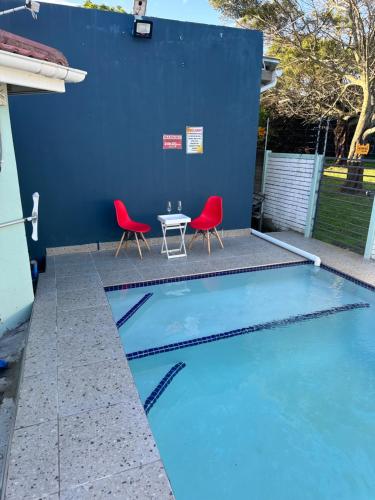una piscina con 2 sillas rojas y una mesa en The legacy BnB, en East London