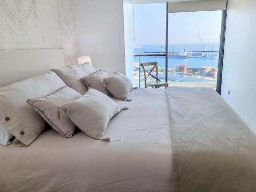 een groot bed met witte kussens en een groot raam bij Dúplex con Terraza y Parking con vista al MarHOM 1118 in Antofagasta
