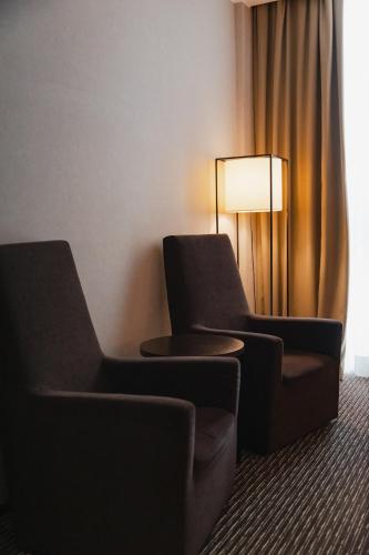 two chairs and a table in a room with a lamp at H2C Hotel Milanofiori in Assago