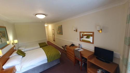 Habitación de hotel con cama y escritorio con TV. en Alton House Hotel en Alton