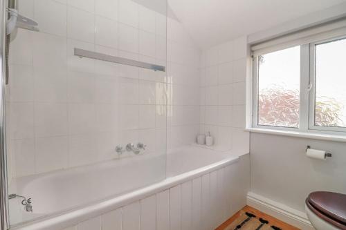 a white bathroom with a tub and a toilet at Quaint 2 bed cottage near North Norfolk Coast - Harpers Cottages in Syderstone