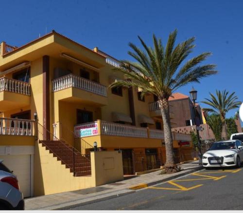 um edifício amarelo com uma palmeira em frente em Apartamentos Trasmallo 1 em La Playa Calera
