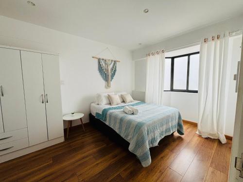 a white bedroom with a bed and a window at Encantador Loft en Lima - Cerca del aeropuerto in Lima