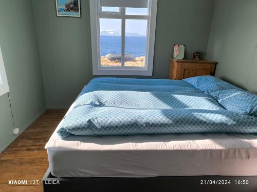 uma cama com um edredão azul num quarto com uma janela em Happy-Cove Guesthouse - by the sea em Bakkafjörður