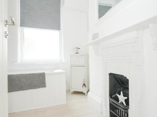 a white bathroom with a fireplace and a window at Lowena Cottage in Looe