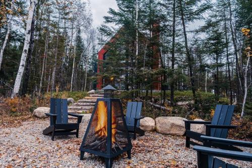 eine Feuerstelle in einem Park mit Stühlen und Bäumen in der Unterkunft Bright chalet with hot tub and indoor sauna in Lac-Superieur