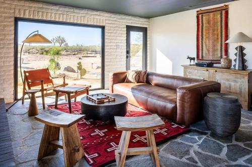 a living room with a leather couch and wooden stools at Escondite: Modern Desert Hideout w Pool + Spa in Landers
