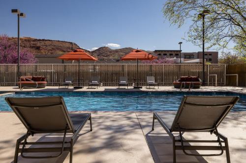 una piscina con sillas y sombrillas junto a una valla en River Canyon Lodge, en Moab