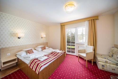 a bedroom with a bed and a chair and a window at Hotel Piroska in Bük