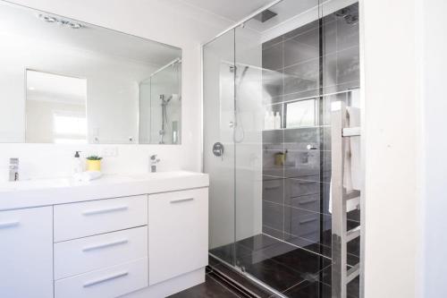 a white bathroom with a shower and a sink at Moffat Beach, Large families & friends unite here! in Caloundra