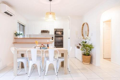 a white kitchen with a table and white chairs at Spacious Apartment, Walk To Kings Beach in Caloundra