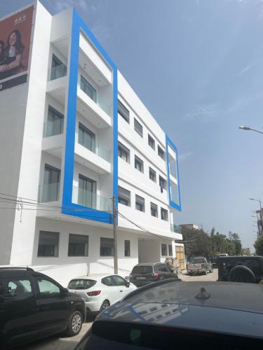 um grande edifício branco com acentos azuis num parque de estacionamento em Sable d’or em Plage de Mehdia