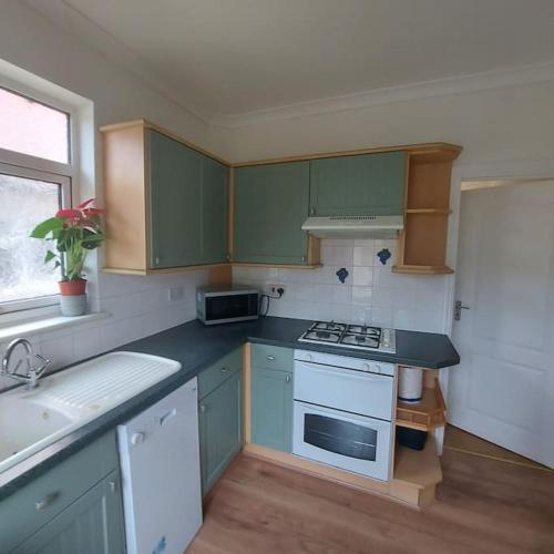 a small kitchen with green cabinets and a sink at Jemima Place semi-detached hse. in Wallington