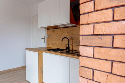 a kitchen with white cabinets and a brick wall at Pokoje i Apartamenty Marek - Niedaleko Plaży in Ostrowo