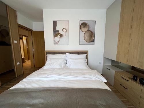 a bedroom with a large white bed and pictures on the wall at Verde Apartman Sokobanja in Soko Banja