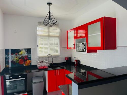 een keuken met rode kasten en een zwart aanrecht bij Charmant appartement coloré proche de la plage in Bouillante