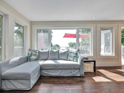 a living room with a gray couch and windows at Wind & Waves - Wellington waterfront with Satellite TV & fire pit in Wellington
