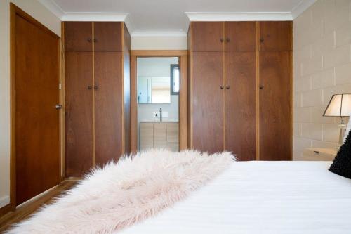 um quarto com uma cama branca e armários de madeira em Cosy & Convenient: WiFi & Parking em Kings Park