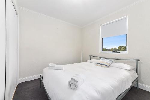 a white bedroom with a bed and a window at Sea Breeze Escape in Bridport