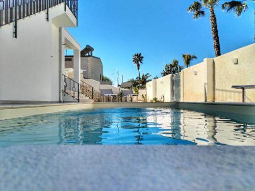 a swimming pool in front of a building with palm trees at Villa Ina Lux in Fontane Bianche