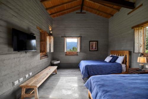 a bedroom with two beds and a tv and a bench at Casa Estrella Malinalco in Malinalco