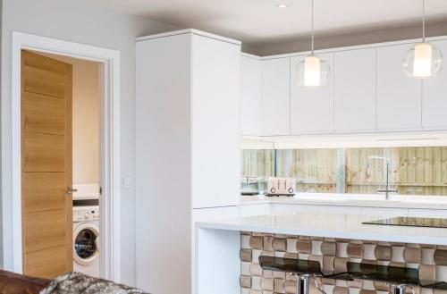 a kitchen with white cabinets and a washer and dryer at Stylish new home with parking - king beds garden in Chichester