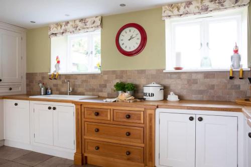 a kitchen with white cabinets and a clock on the wall at Stunning Cottage in South Downs National Park in Eartham