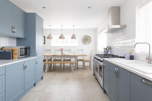 a kitchen with blue cabinets and a dining room at Beach house for 10 with hot tub & garden in West Wittering