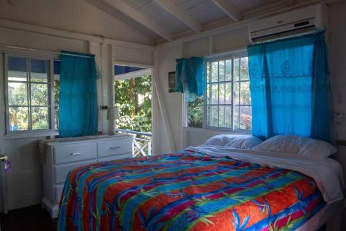 a bedroom with a bed with blue curtains and windows at Relax in Paradise: Spectacular house In Negril-Indika in Negril