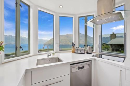 a kitchen with white cabinets and windows with a view at Ruby's Fernhill Vista in Queenstown