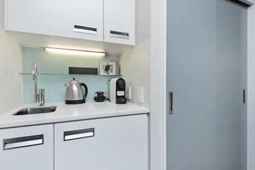 uma cozinha com armários brancos e um lavatório com uma chaleira. em Stunning 1 Bedroom Studio Apartment em Queenstown